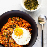 Kimchi tuna fried rice served in a black pasta bowl. Also next to it is a spoon and a bowl of dried seaweed furikake.