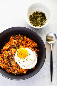 Kimchi tuna fried rice served in a black pasta bowl. Also next to it is a spoon and a bowl of dried seaweed furikake.