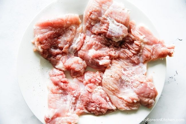 Flattened and scored raw chicken thigh fillets on a white plate.