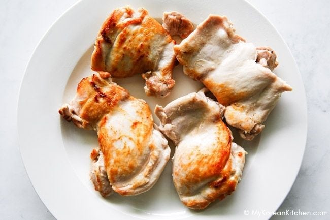 Golden brown pan fried chicken thigh fillets on a white plate.