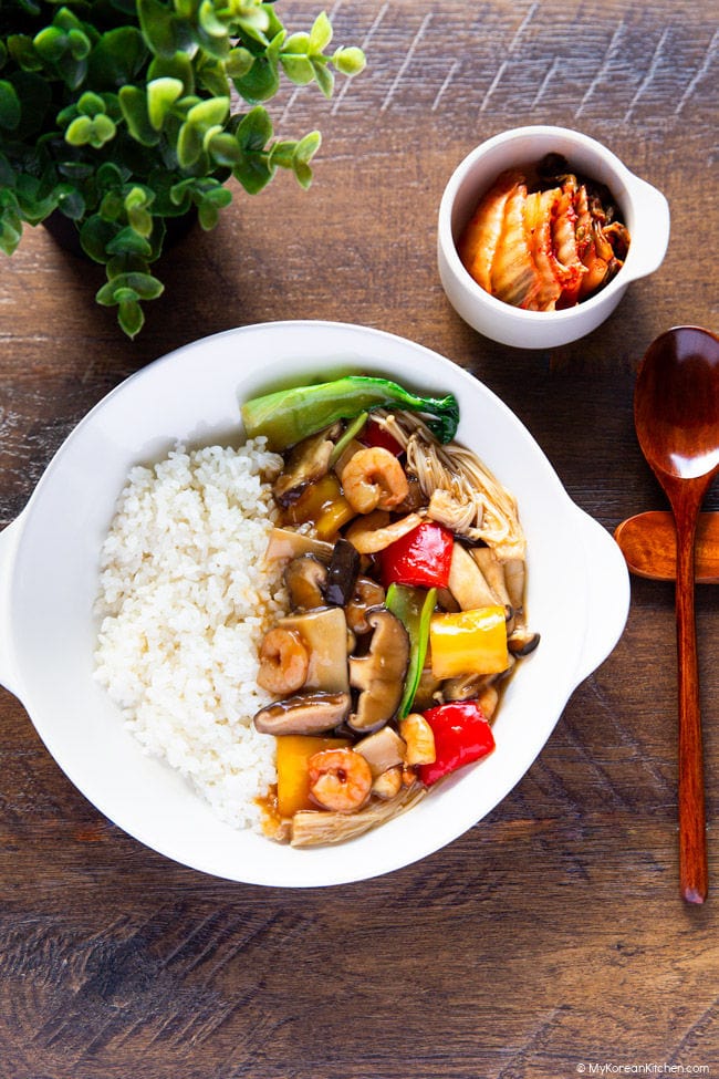 Mushroom and rice on a plate with a side of kimchi and a wooden spoon.