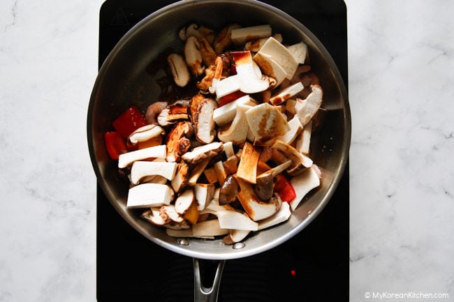 Continuing to stir-fry mushrooms and other ingredients in a pan after adding sauce.