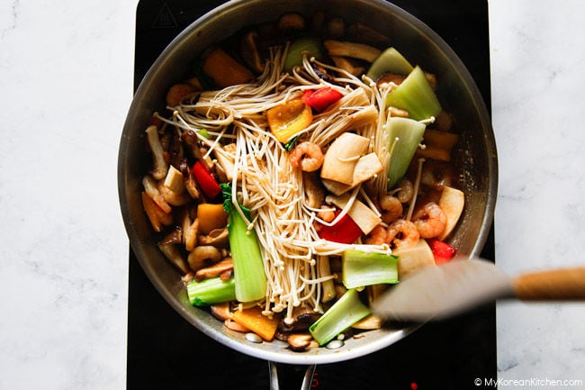 Enoki mushrooms mixed with other mushrooms and vegetables in a stainless steel pan.