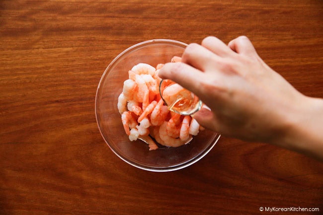 Pouring rice wine into a bowl of cleaned shrimps for marinating.