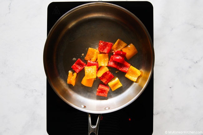 Cooking chopped red and yellow bell peppers in a stainless steel pan.