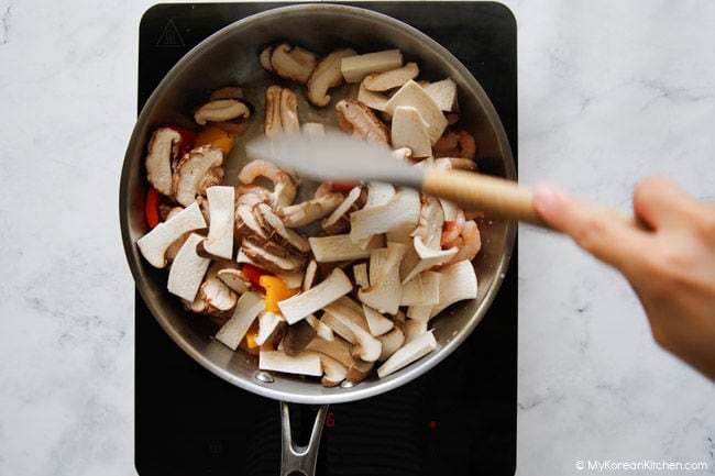 Stir-frying mushrooms and shrimp with vegetables in a stainless steel pan.