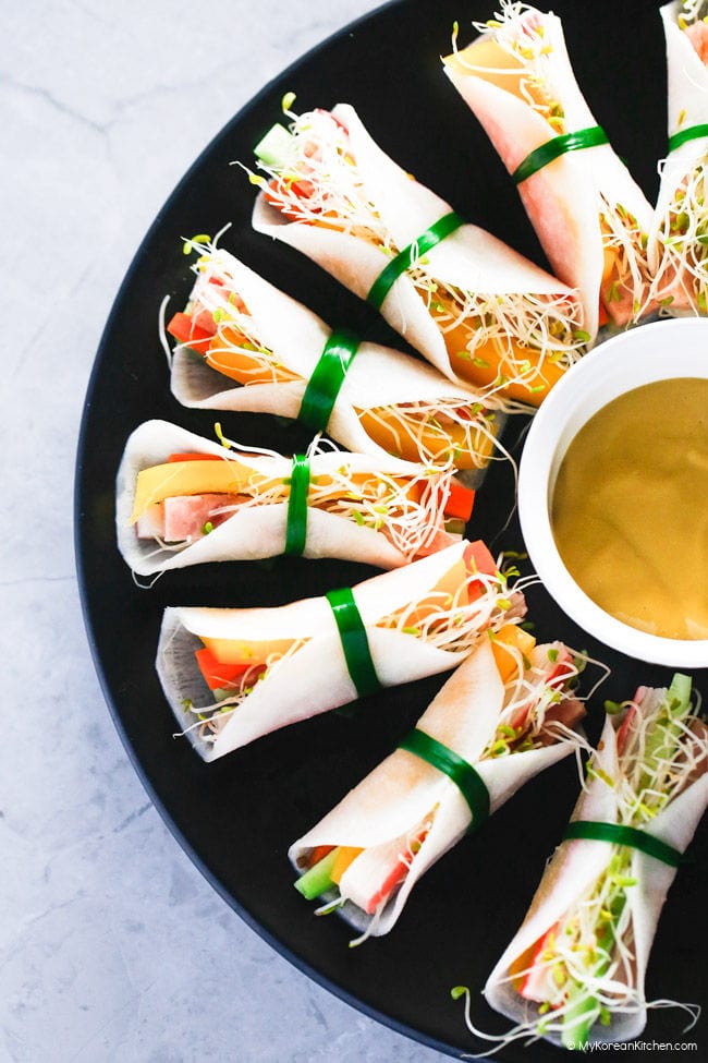 Pickled radish wraps served on a black plate with dipping sauce in the middle.