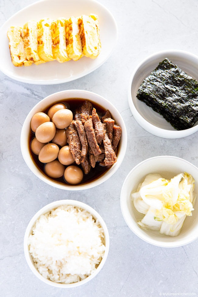 Jangjorim served with a bowl of white rice and other side dishes such as rolled egg omelette, dried seaweed and white kimchi.