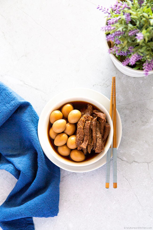 Soy braised beef and quail eggs served in a bowl, a pair of chopsticks on the side.