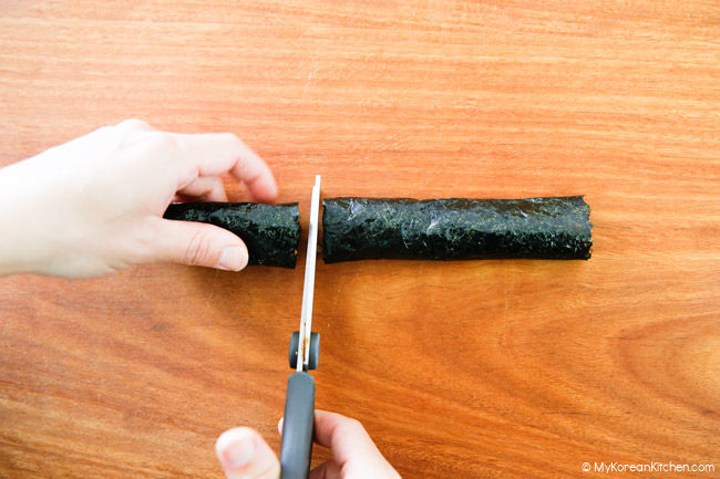 Cutting gimmari over a cutting board with a pair scissors.