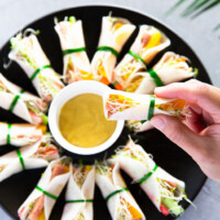 Holding a pickled radish wrap in one hand, in the background, radish wraps are served on a black plate.