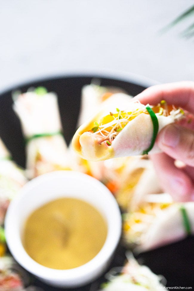 Holding a pickled radish wrap with a sauce dipping sauce in one hand.