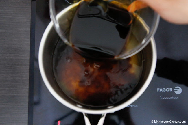 Pouring soy sauce over a pot of beef broth.