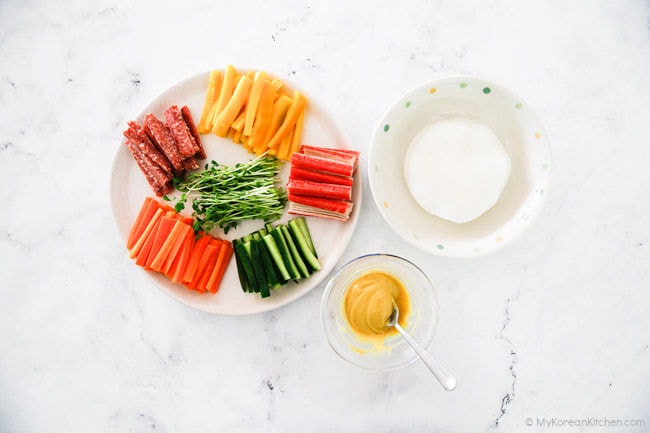 Prepared pickled radish wrap ingredients on a marble background.