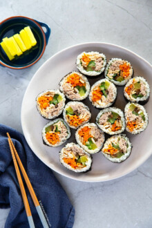 Sliced tuna kimbap served on a white plate with yellow pickled radish.