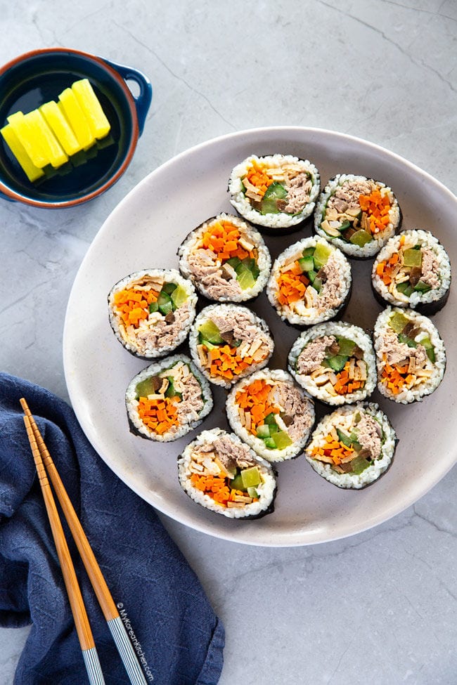 Sliced tuna kimbap served on a white plate with yellow pickled radish.