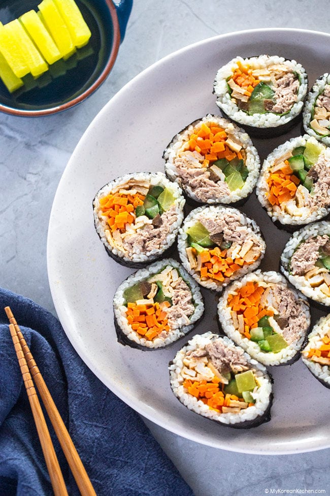 Sliced tuna kimbap served on a white plate with yellow pickled radish.