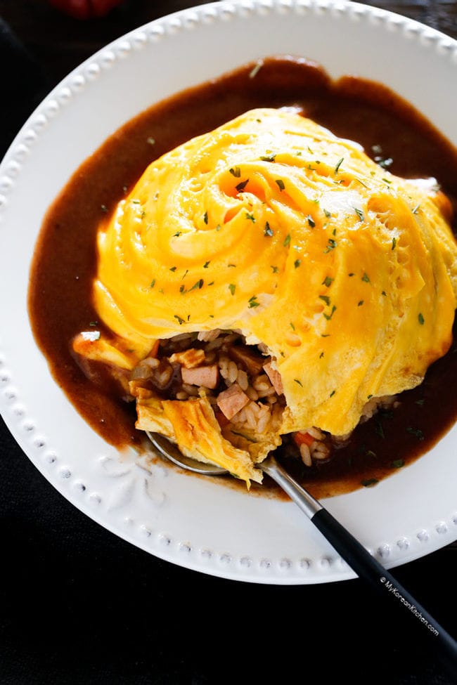 Omelette rice served on a white plate. Spoon cut a corner of the omurice.