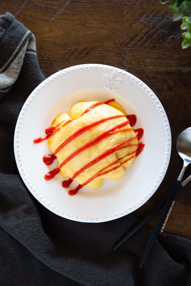Omelette rice served on a white plate with drizzled ketchup