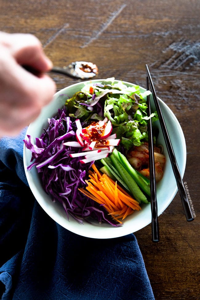 Adding bibim guksu sauce over assorted salad