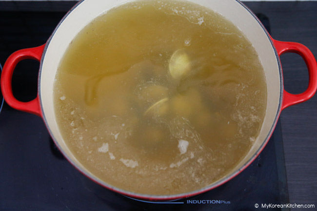 Dak kalguksu broth is boiling in a red pot with little neck clams inside.