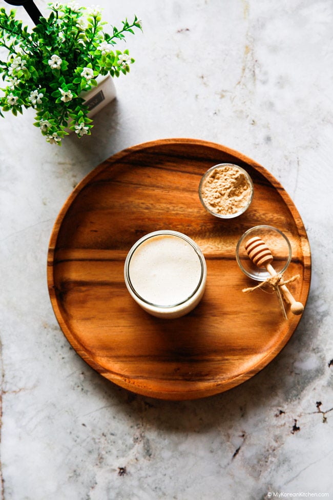 Top down image of a misugaru latte on a wooden tray, with a small bowl of misugaru powder and a decorative honey spoon alongside.