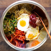 bibimbap ingredients in a large stainless steel bowl, including a sunny side egg, zucchini, spicy radish salad, bean sprout salad, and gochujang.