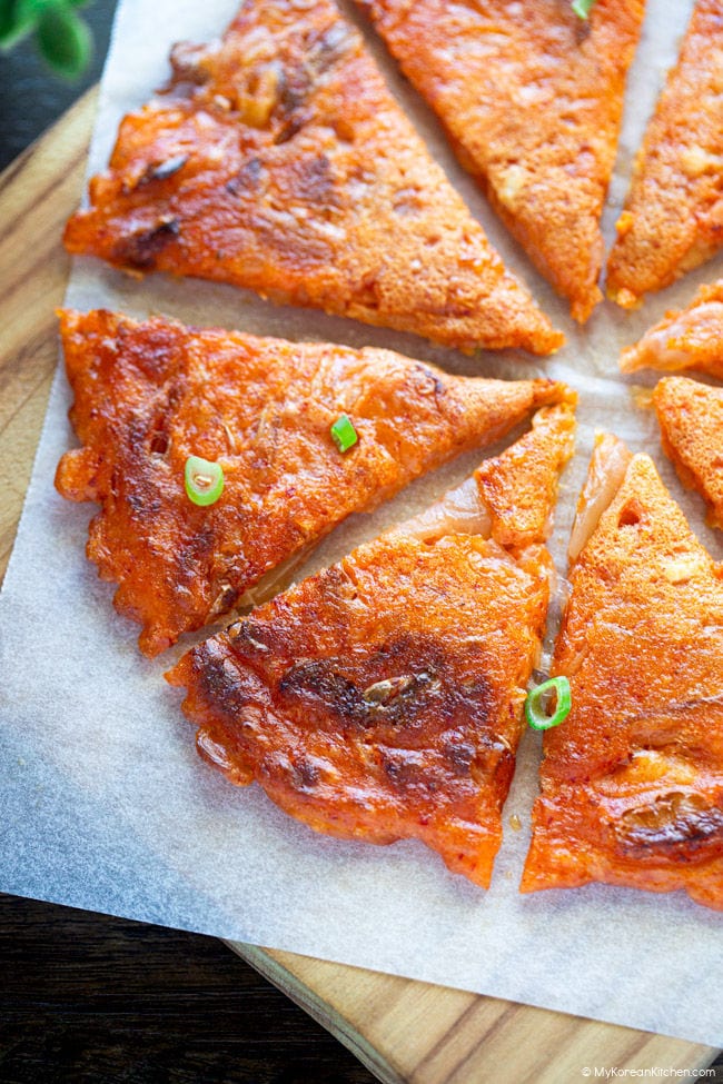 Sliced kimchi pancake into bite-sized pieces, served on a wooden board.