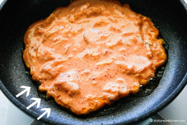 Crispy kimchi pancake sizzling in a pan over medium heat