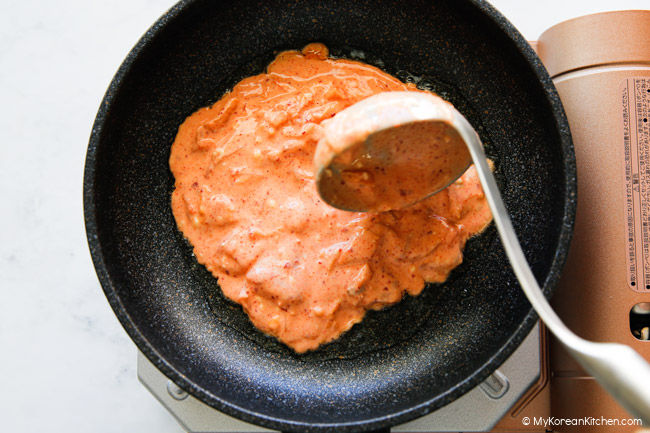 Placing a scoop of kimchi pancake batter into a pan using a ladle