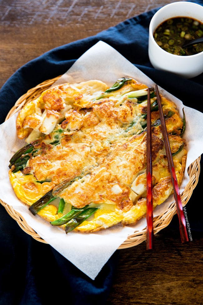 seafood pancake served on white waxed paper and chopsticks is laid on top of the pancake
