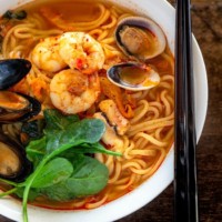 A bowl of jjampong topped with prawns, mussels and littleneck clams.