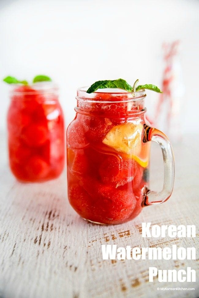 Two glass jugs of Korean watermelon punch, filled with watermelon and ice.