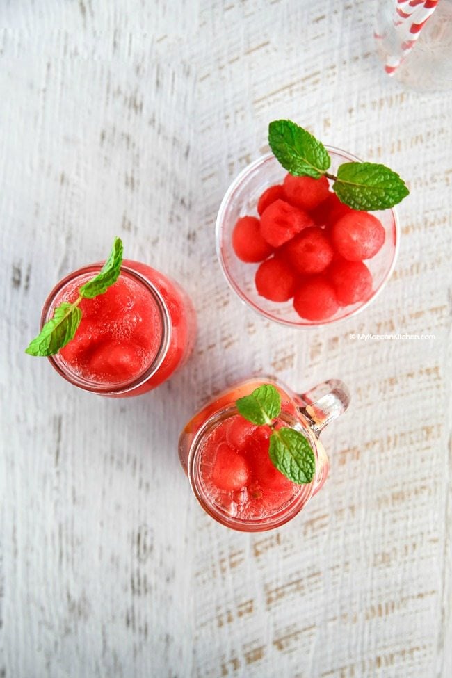 Three glass jugs filled with Korean watermelon punch, topped with fresh mint leaves.