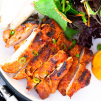 spicy gochujang chicken served on a white plate with green salad