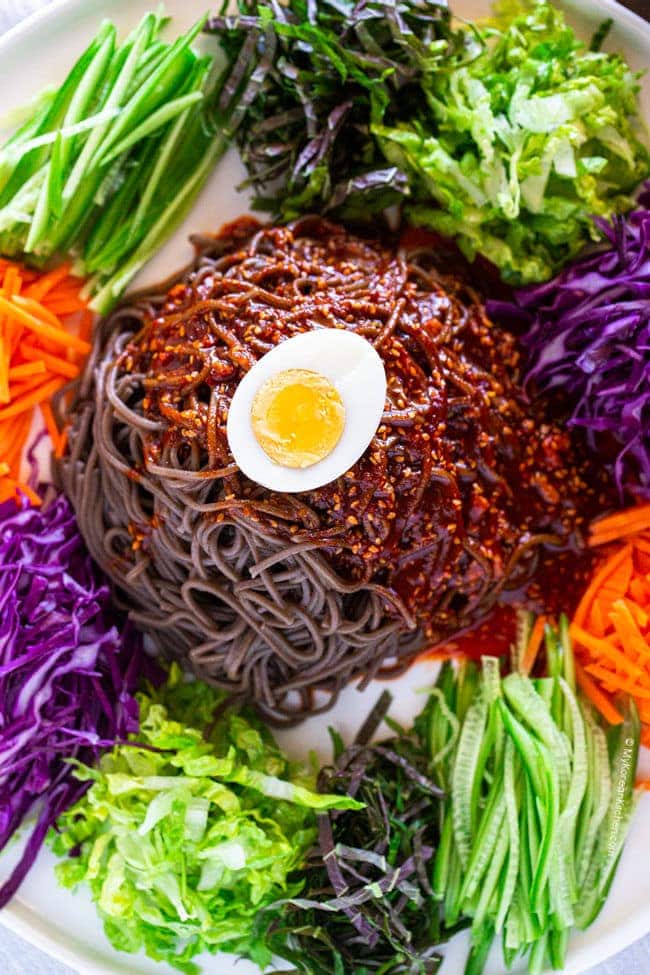 close up photo of spicy noodle salad featuring halved boiled egg on top of noodles