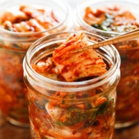 Holding kimchi with wooden chopsticks over a glass kimchi jar