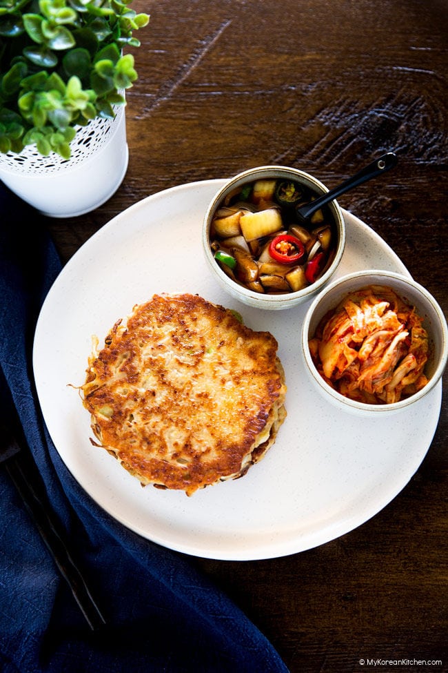 Bindaetteok served on a white plate with pickled onion and kimchi.