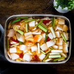 A vertical photo of nabak kimchi in a stainless steel container.