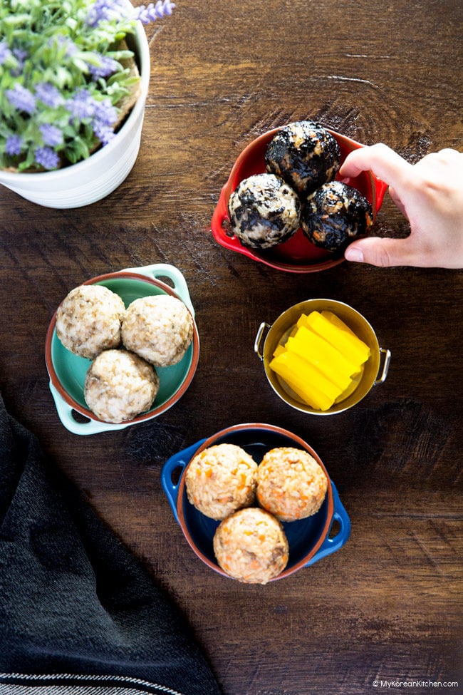 A spread of Korean rice balls. A finger reaches out to one of them.