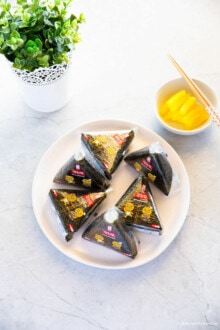Six triangle kimbap served on a plate, yellow pickled radish in the background