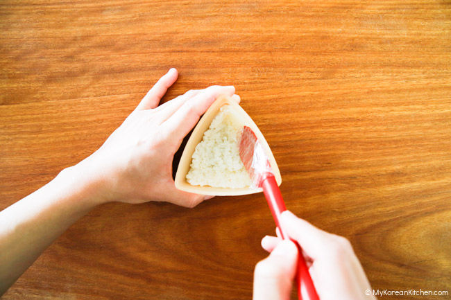 Pressing the rice with a red jar spatula in the triangle kimbap mold.