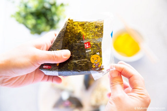 Pulling down the plastic film in the right-hand corner while holding down the triangle kimbap with my left hand.