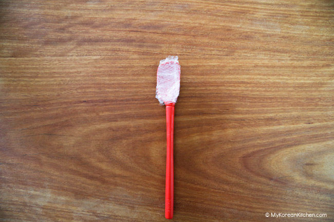 Red jar spatula on the wooden board.