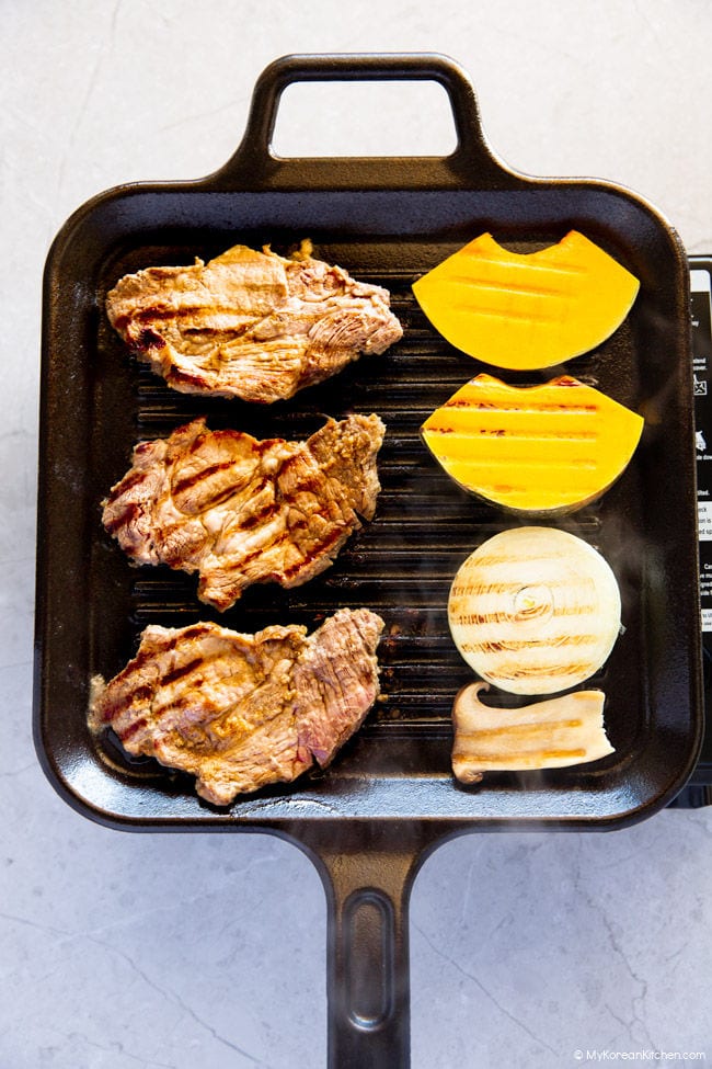 Cooking Korean BBQ Pork, sliced king oyster mushrooms, onion rings, and pumpkin on a griddle.
