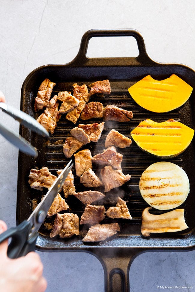 Chopping Korean BBQ Pork with a pair of scissors on a griddle.