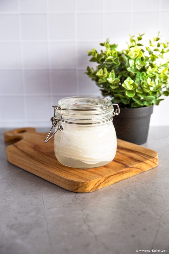 Pickled sliced radishes in a glass jar. A black pot of plant near the wooden cutting board.