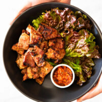 Holding a black bowl filled with Korean BBQ Pork, lettuce, and spicy dipping sauce with two hands.