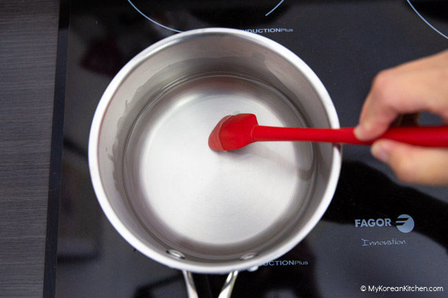 Stirring the pickling brine with a red spatula in a saucepan.