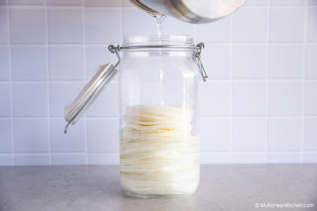 Pouring pickling brine over sliced radish in a glass jar.